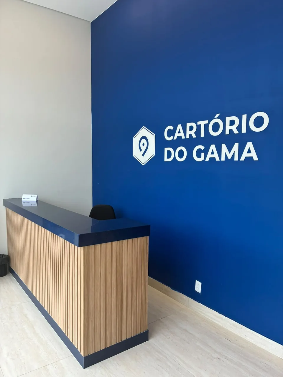 Balcão de recepção ripado em madeira diante de parede azul com logotipo