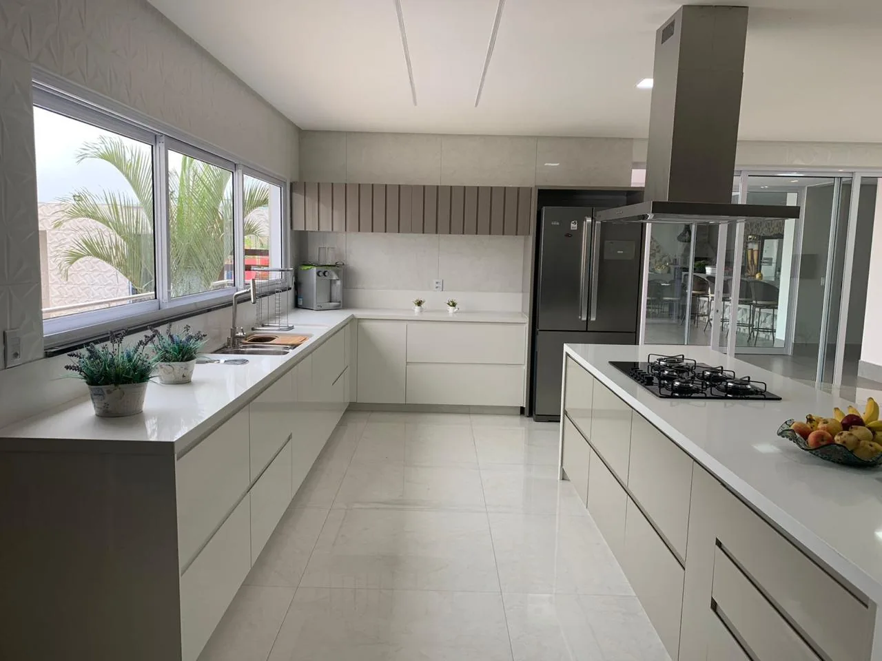Cozinha em U com armários claros, cooktop na ilha e geladeira de inox