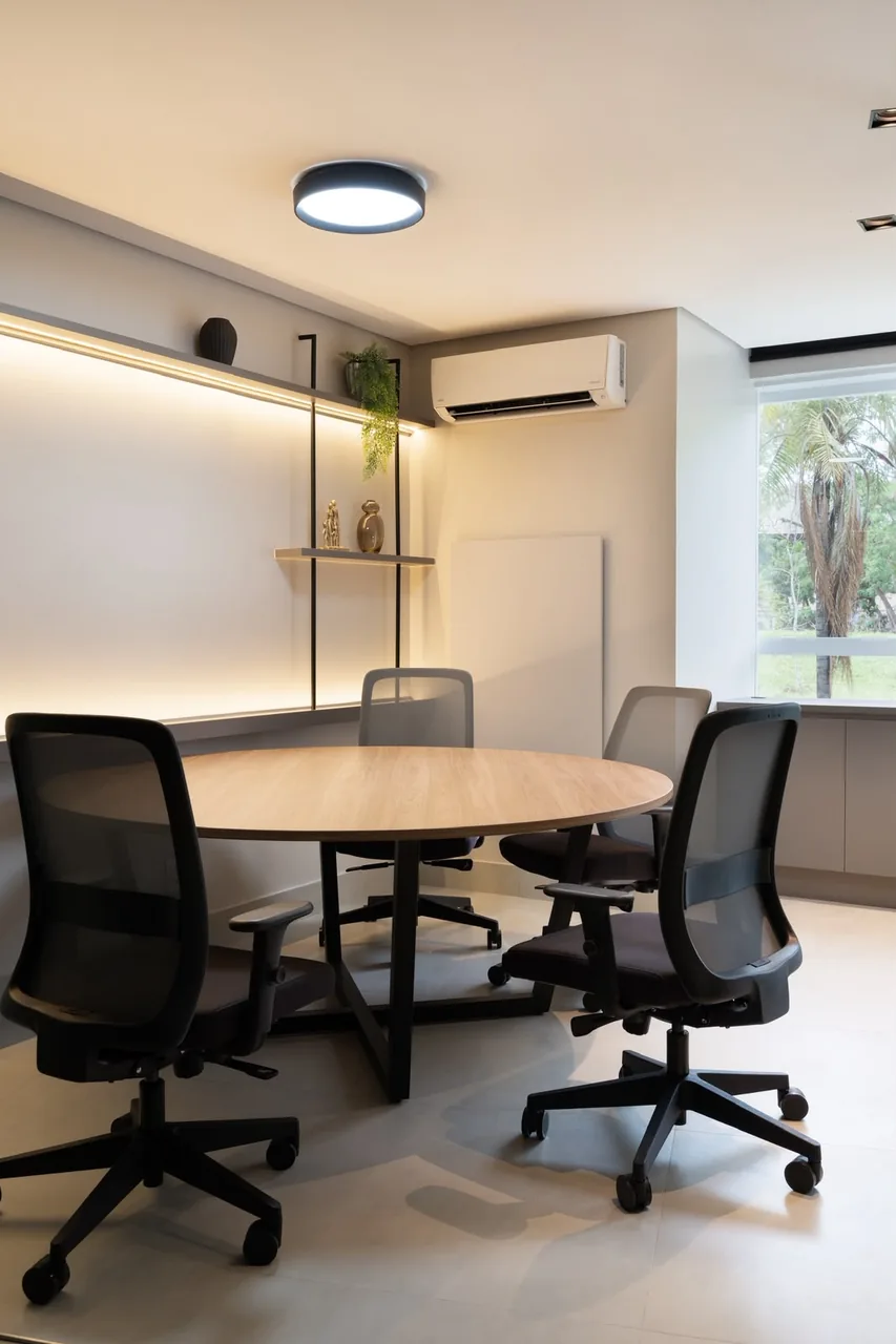 Sala de reunião com mesa redonda de madeira e armário baixo ao fundo