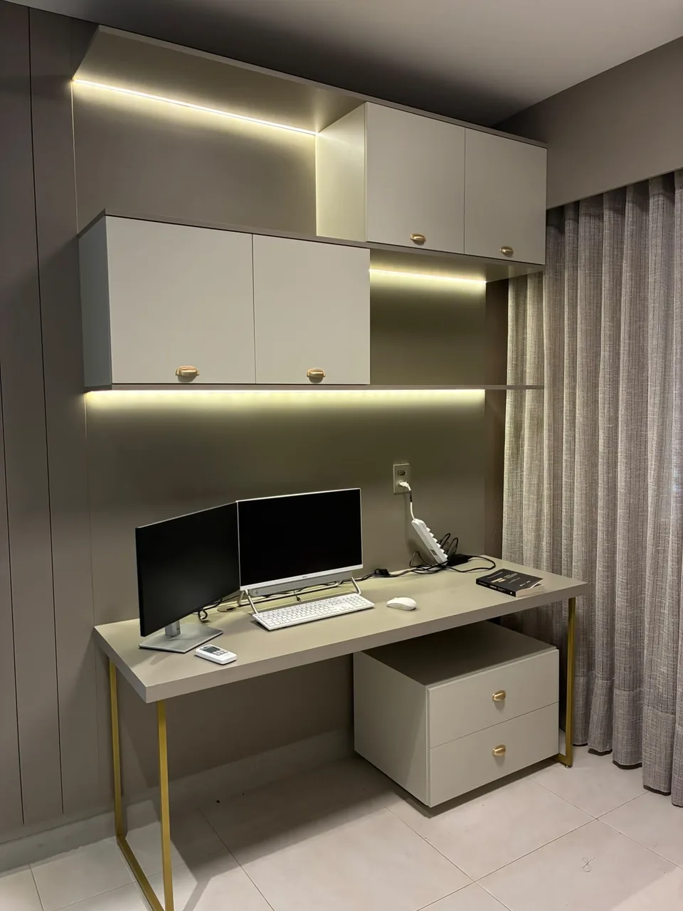 Home office com bancada, gaveteiro e iluminação embutida na prateleira
