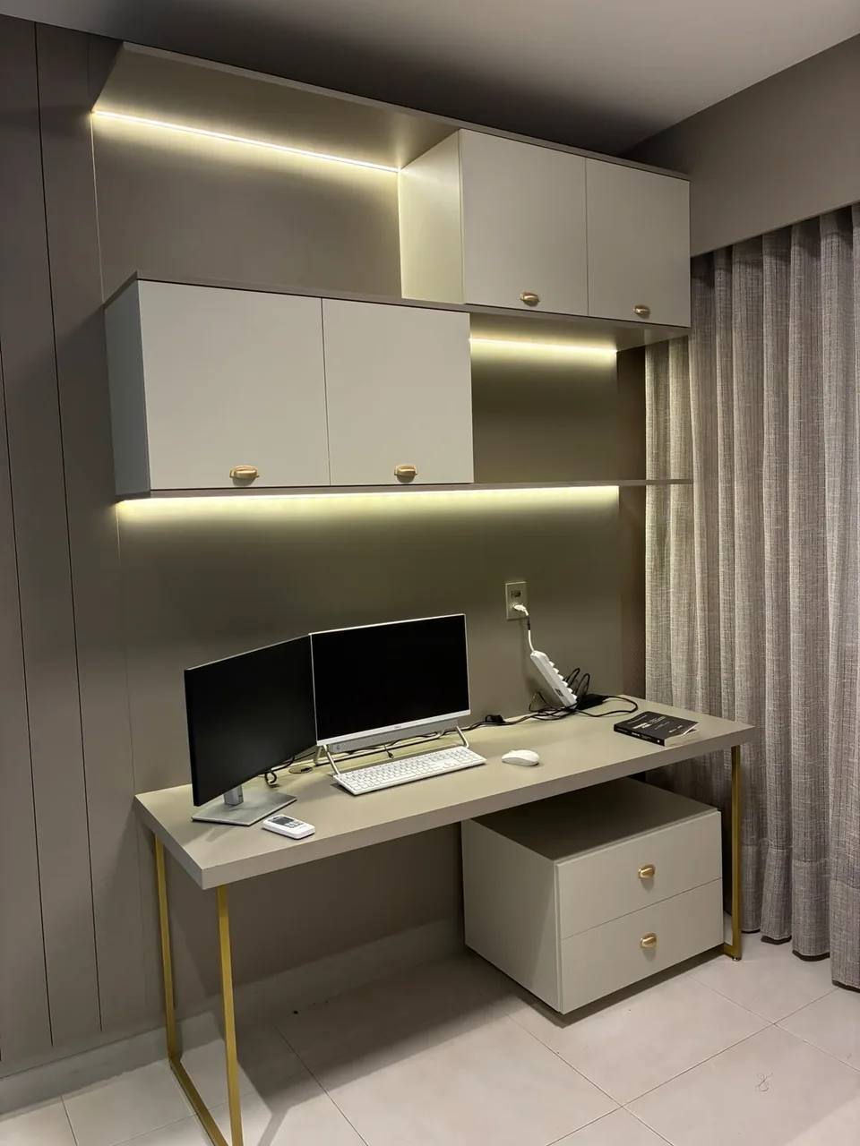 Home office integrado ao quarto, com cortina e armário aéreo iluminado