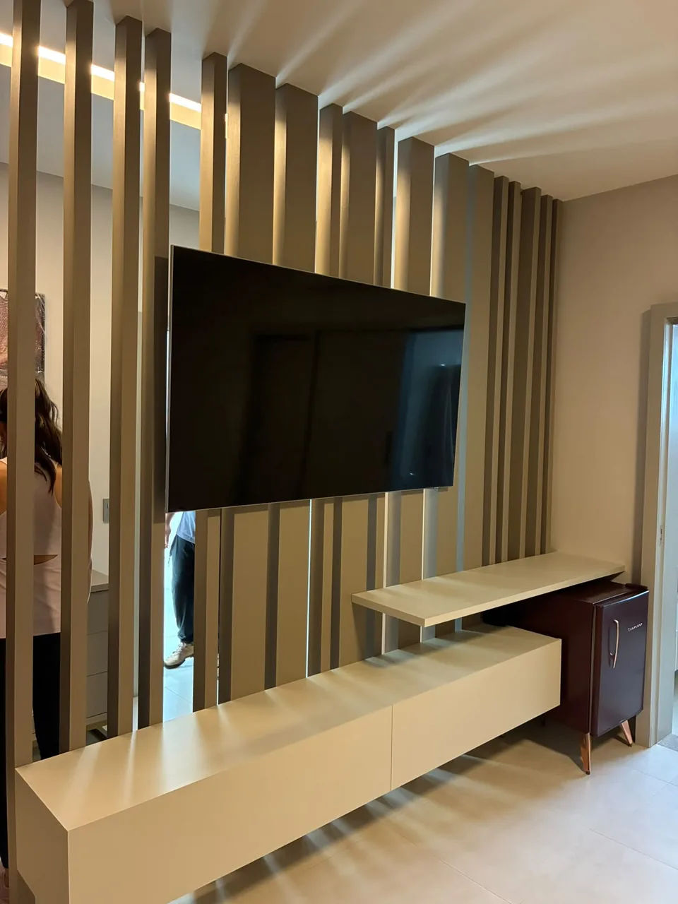 Painel ripado dourado com televisão e rack suspenso na sala de estar