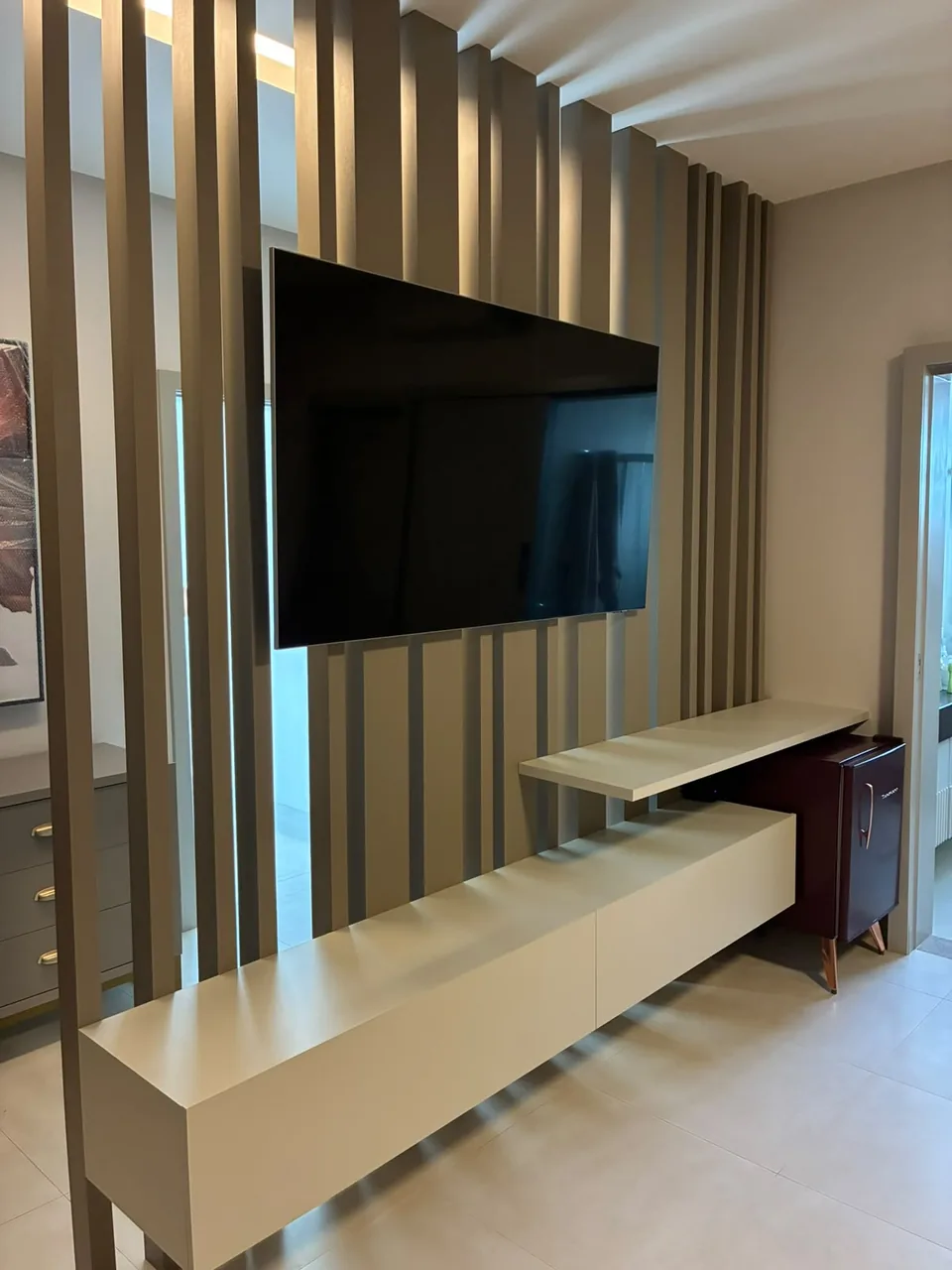Sala de estar com painel ripado dourado, rack suspenso e vão de passagem