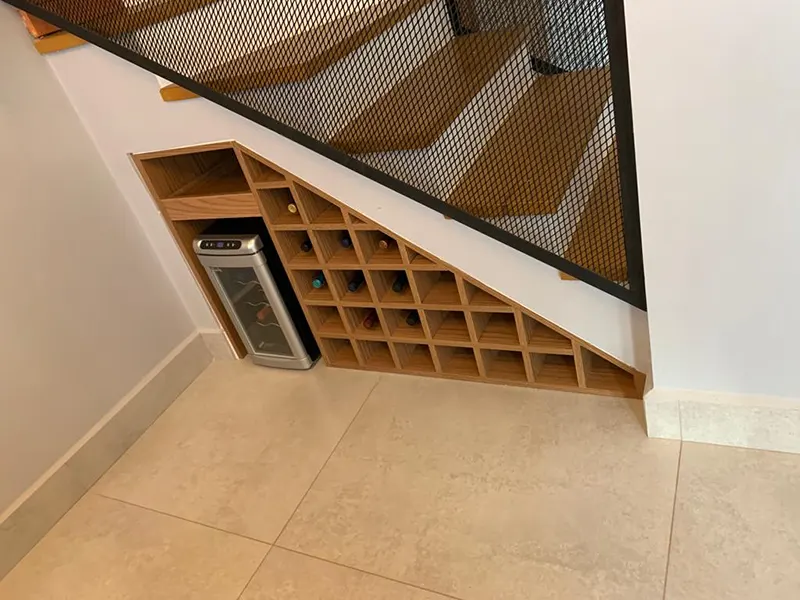 Adega sob a escada, com nichos diagonais em madeira para garrafas