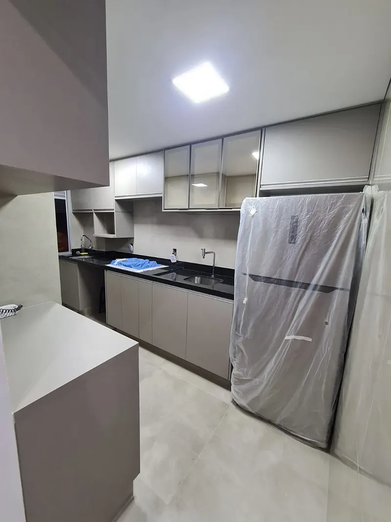Cozinha em corredor com armários cinza, bancada escura e geladeira embutida