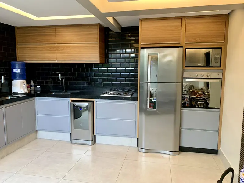 Cozinha com revestimento preto, armários brancos e torre de forno e micro-ondas