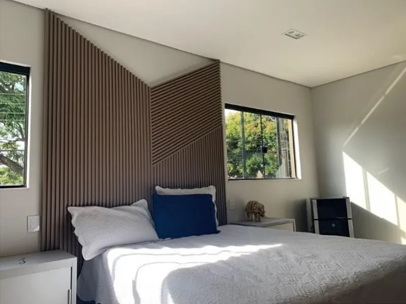Quarto de casal com painel ripado escuro atrás da cama e janelas laterais